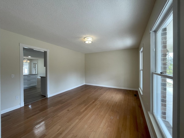 empty room featuring a textured ceiling, wood finished floors, and baseboards