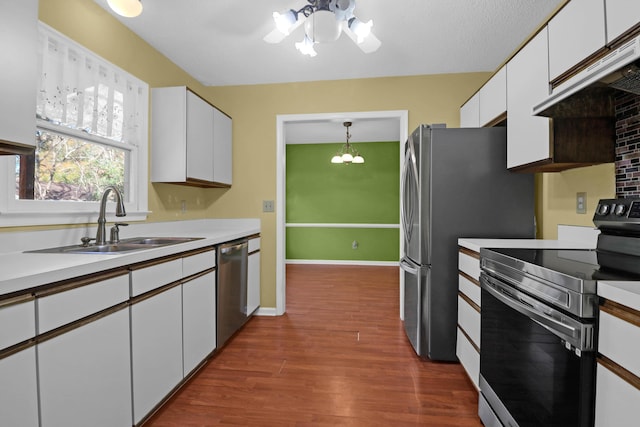 kitchen featuring stainless steel appliances, sink, exhaust hood, an inviting chandelier, and white cabinetry