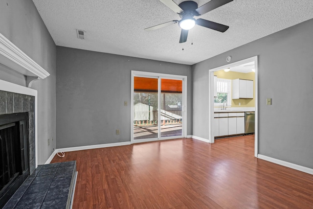 unfurnished living room with a tiled fireplace, ceiling fan, hardwood / wood-style floors, and a textured ceiling