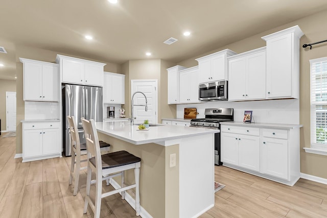 kitchen with stainless steel appliances, light wood-type flooring, sink, an island with sink, and white cabinets