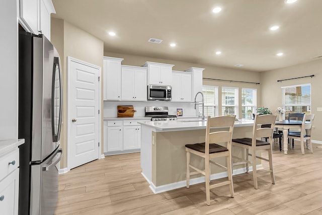 kitchen featuring stainless steel appliances, sink, an island with sink, white cabinetry, and light hardwood / wood-style flooring