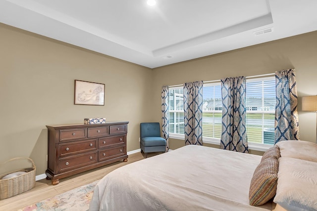 bedroom with light hardwood / wood-style floors and a raised ceiling