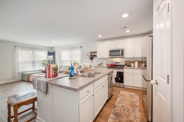 kitchen featuring appliances with stainless steel finishes, a sink, light wood-style floors, white cabinets, and open floor plan