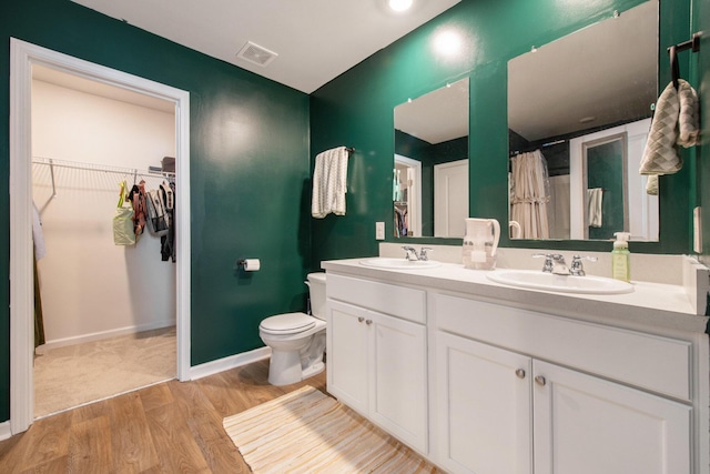 bathroom featuring wood finished floors, toilet, a spacious closet, double vanity, and baseboards