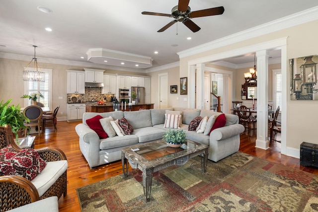 living room with ceiling fan with notable chandelier, ornamental molding, decorative columns, and dark hardwood / wood-style floors