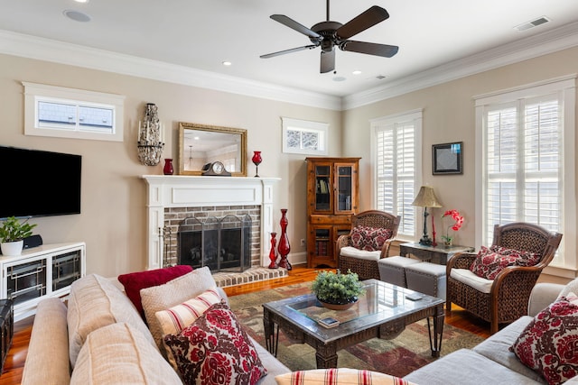 living room featuring a brick fireplace, hardwood / wood-style floors, crown molding, and ceiling fan