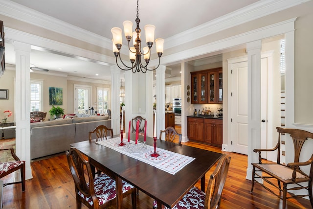 dining room featuring dark hardwood / wood-style flooring, crown molding, decorative columns, and bar area