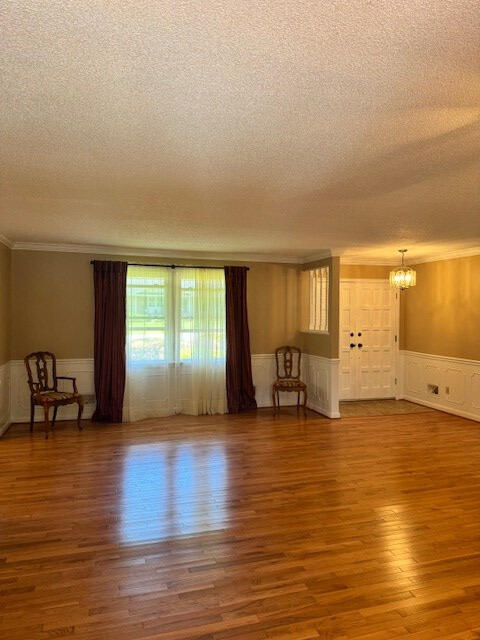 1153 Cherokee Dr, Manning, SC 29102 - unfurnished living room with a textured ceiling, a chandelier, a wainscoted wall, ornamental molding, and wood finished floors