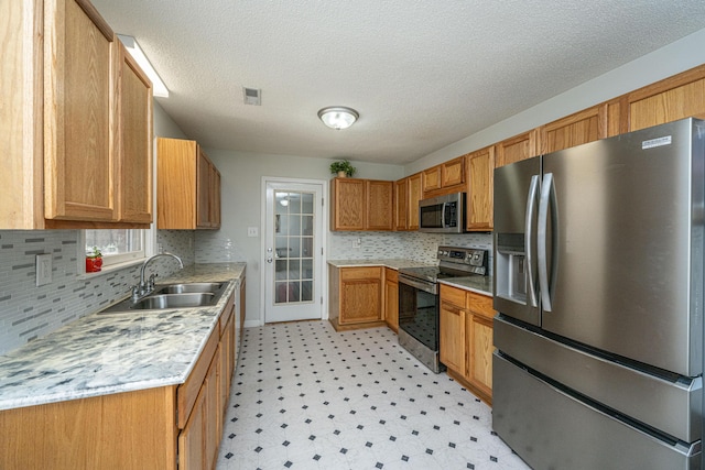 kitchen with sink, tasteful backsplash, a textured ceiling, stainless steel appliances, and light stone countertops