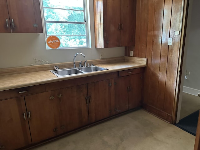 kitchen with a sink, light colored carpet, brown cabinetry, and light countertops