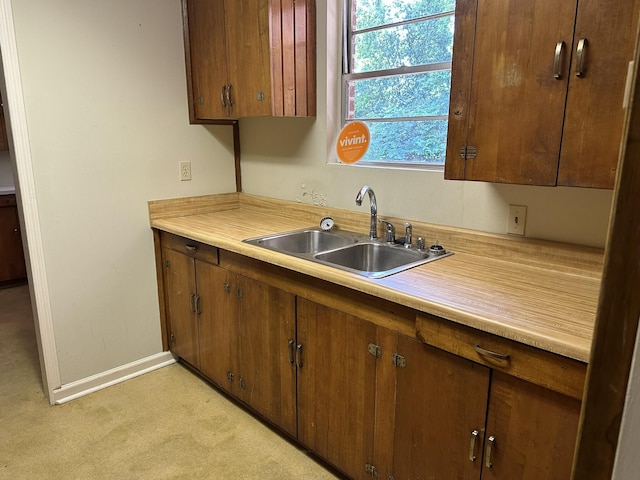 kitchen with brown cabinets, a sink, baseboards, light countertops, and light carpet