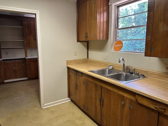 kitchen featuring a sink, brown cabinets, light colored carpet, light countertops, and baseboards