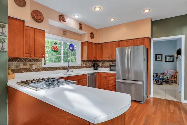 kitchen featuring sink, stainless steel appliances, kitchen peninsula, light hardwood / wood-style floors, and decorative backsplash