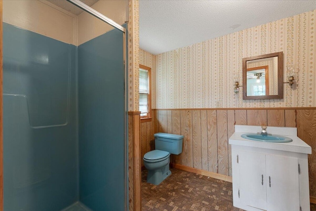 bathroom featuring toilet, wooden walls, vanity, a textured ceiling, and a shower with shower door