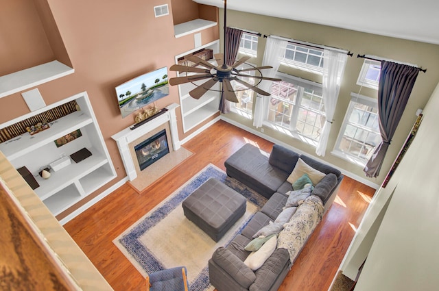 living room featuring ceiling fan, a premium fireplace, high vaulted ceiling, light hardwood / wood-style flooring, and built in features