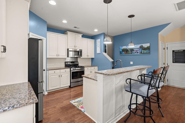 kitchen featuring decorative light fixtures, stainless steel appliances, a kitchen bar, white cabinets, and dark hardwood / wood-style floors