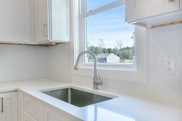 interior details with white cabinetry, decorative backsplash, a sink, and light countertops