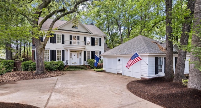 view of front of house with a garage, concrete driveway, an outbuilding, a balcony, and roof with shingles