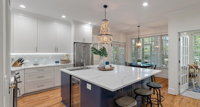 kitchen with an inviting chandelier, high quality appliances, white cabinets, a kitchen island with sink, and wine cooler