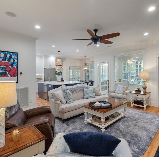 living room featuring ornamental molding, visible vents, ceiling fan, and light wood-style flooring
