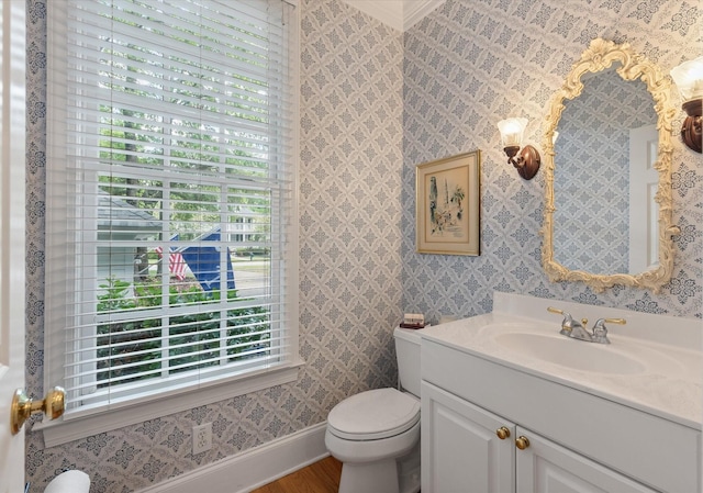 bathroom featuring vanity, baseboards, wallpapered walls, toilet, and wood finished floors