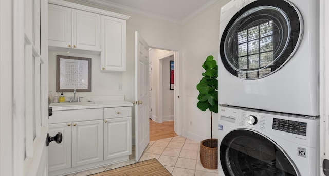 clothes washing area featuring baseboards, stacked washer and dryer, light tile patterned floors, crown molding, and a sink