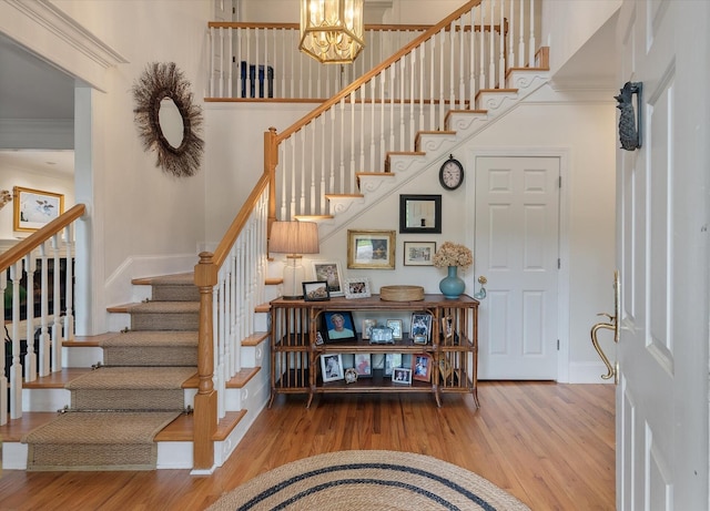 staircase featuring wood finished floors, a notable chandelier, and ornamental molding