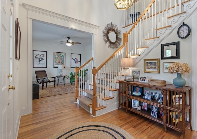 staircase featuring crown molding, wood finished floors, ceiling fan with notable chandelier, and baseboards