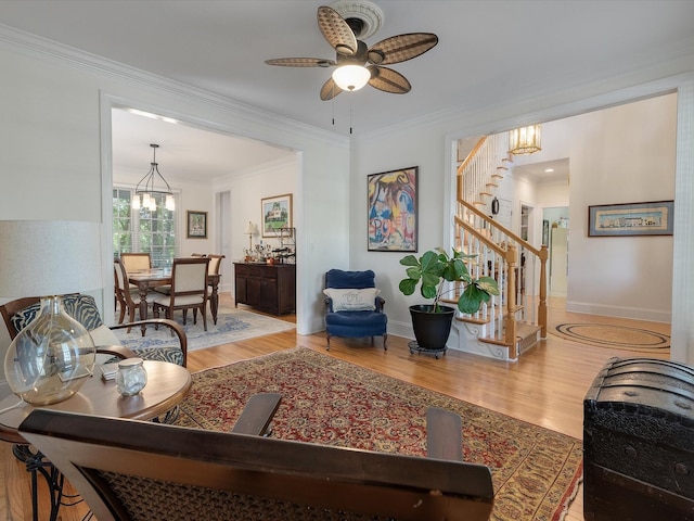 living area with baseboards, stairway, crown molding, ceiling fan with notable chandelier, and wood finished floors
