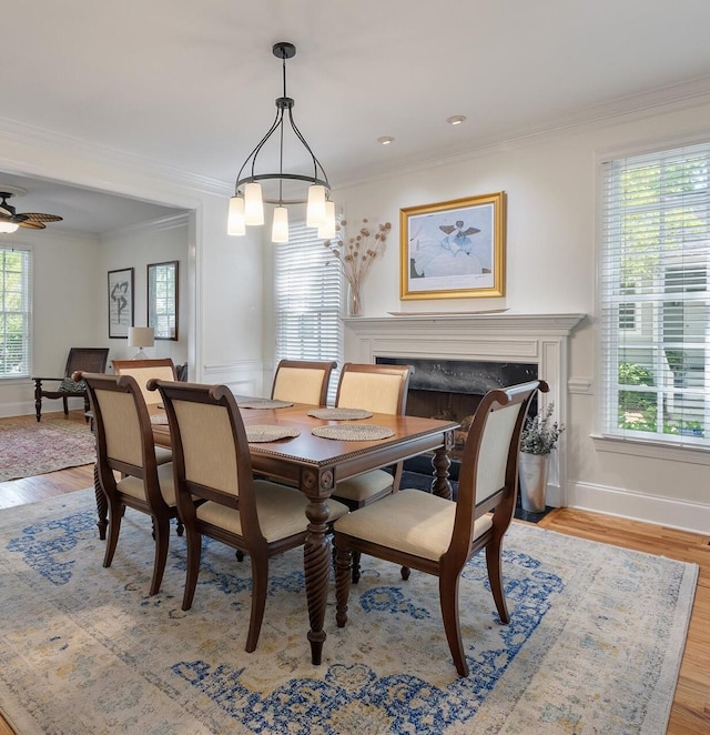 dining room featuring crown molding, baseboards, light wood finished floors, and a fireplace