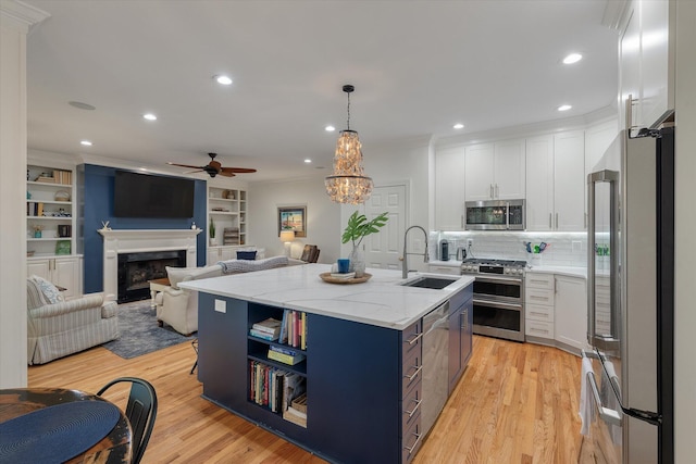 kitchen featuring an island with sink, white cabinets, ceiling fan, stainless steel appliances, and a sink