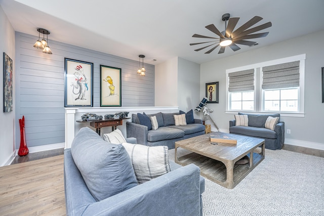 living room featuring ceiling fan, wood walls, and light wood-type flooring