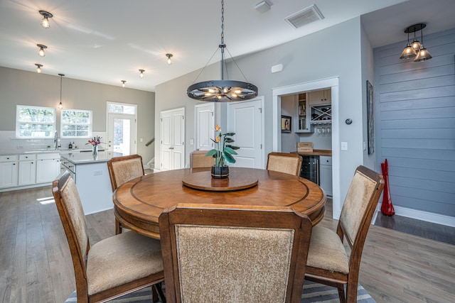 dining area with hardwood / wood-style flooring, a notable chandelier, wine cooler, and wooden walls