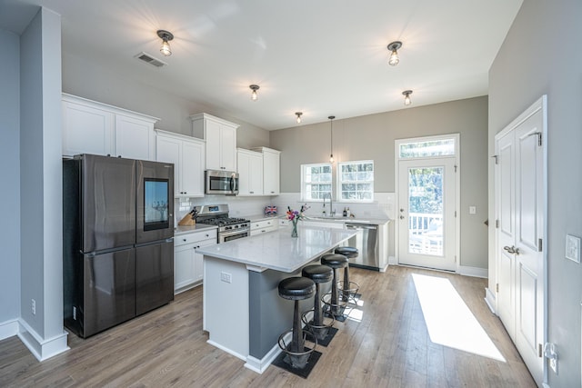 kitchen featuring decorative light fixtures, a kitchen island, white cabinets, and appliances with stainless steel finishes