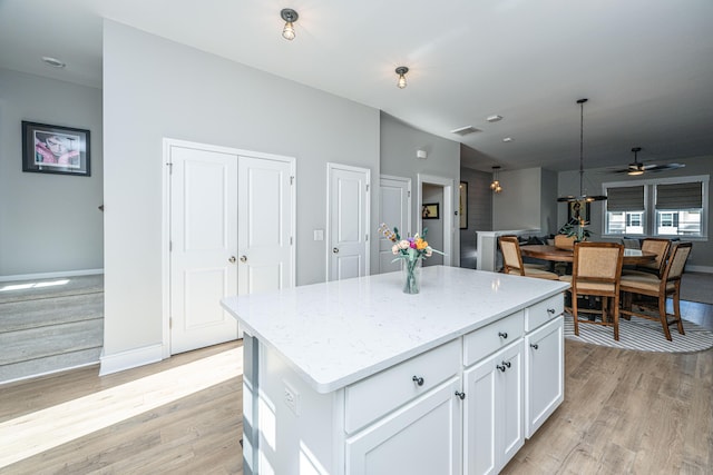 kitchen with white cabinetry, light stone countertops, light hardwood / wood-style floors, and a center island