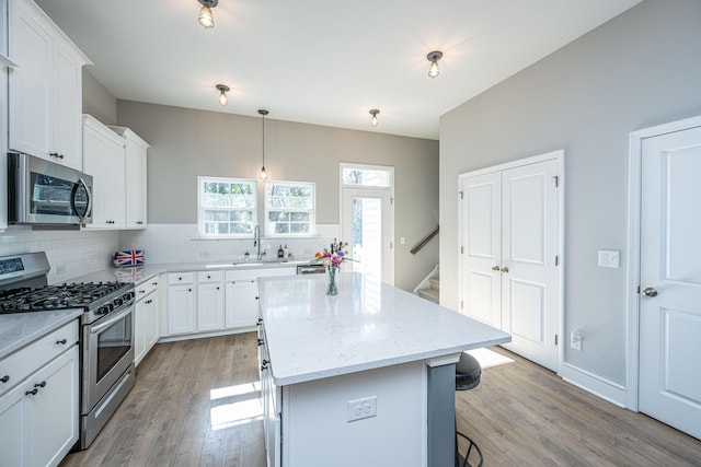 kitchen featuring white cabinetry, decorative light fixtures, a center island, appliances with stainless steel finishes, and light stone countertops