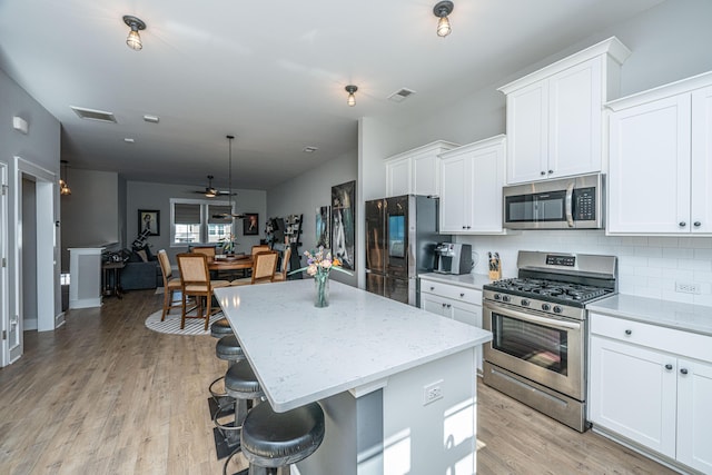 kitchen featuring a kitchen island, appliances with stainless steel finishes, white cabinets, and a kitchen bar