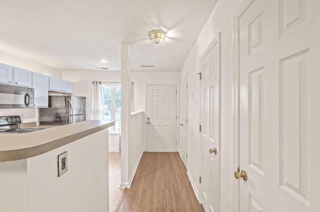 kitchen with kitchen peninsula, range, light wood-type flooring, and black fridge