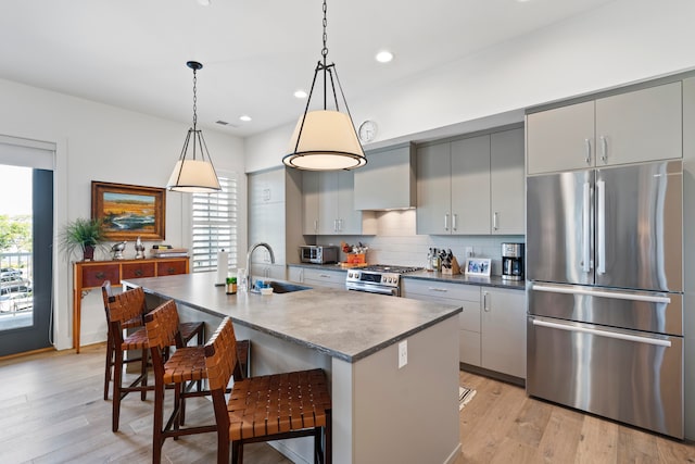 kitchen with a kitchen island with sink, a breakfast bar, stainless steel appliances, gray cabinets, and light wood-type flooring