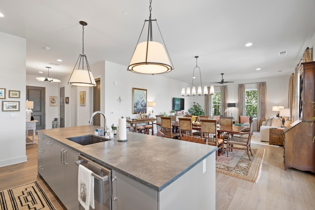 kitchen featuring a center island with sink, dishwasher, light hardwood / wood-style floors, hanging light fixtures, and sink