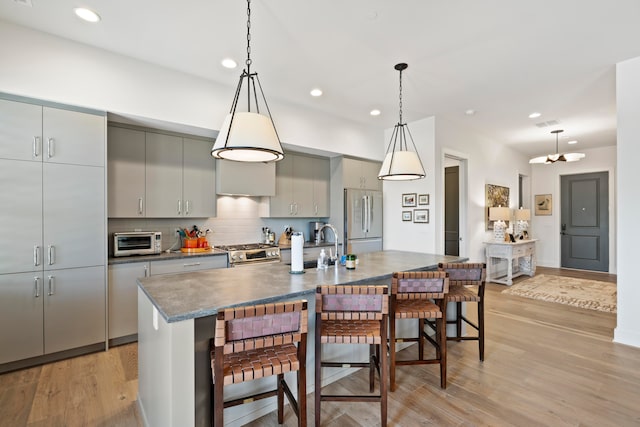 kitchen with decorative light fixtures, appliances with stainless steel finishes, a kitchen island with sink, and light hardwood / wood-style flooring