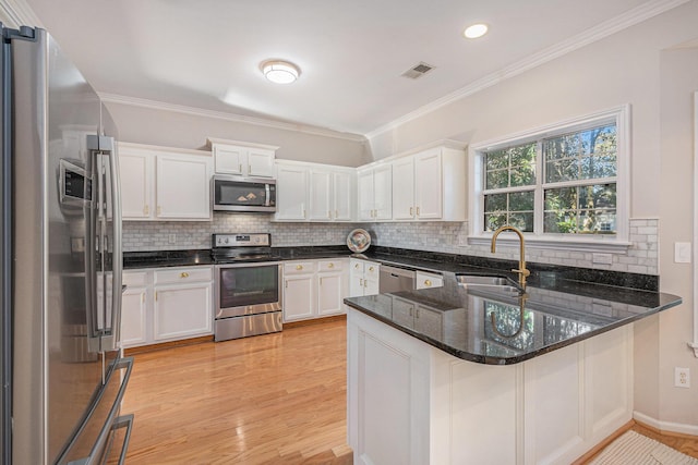 kitchen featuring sink, dark stone counters, kitchen peninsula, stainless steel appliances, and white cabinets