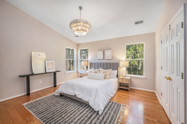 bedroom featuring a notable chandelier, light hardwood / wood-style flooring, a textured ceiling, and vaulted ceiling