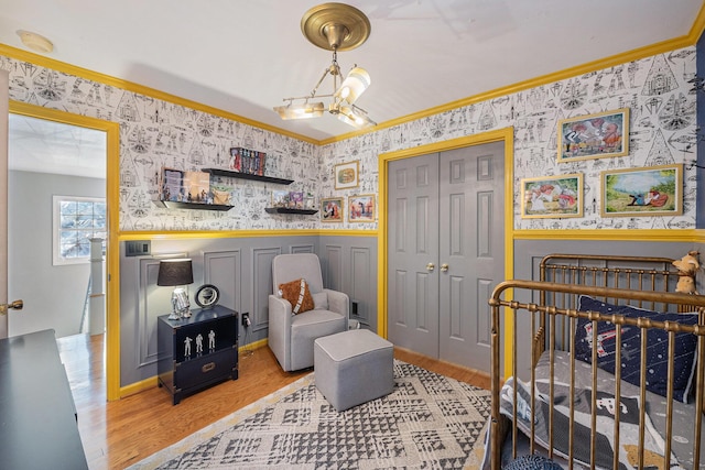 bedroom with an inviting chandelier, ornamental molding, a crib, and light wood-type flooring