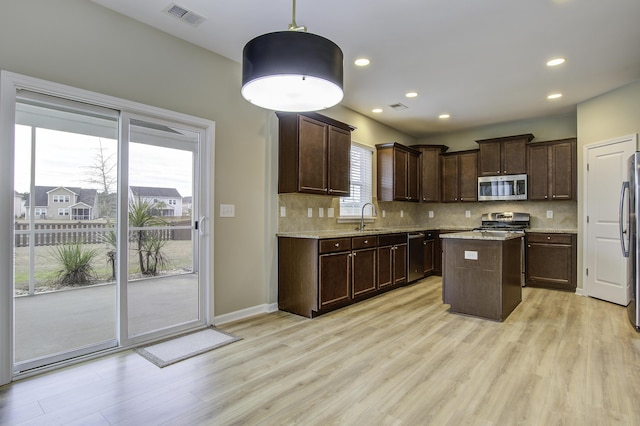 kitchen with a center island, hanging light fixtures, light wood-type flooring, appliances with stainless steel finishes, and dark brown cabinets