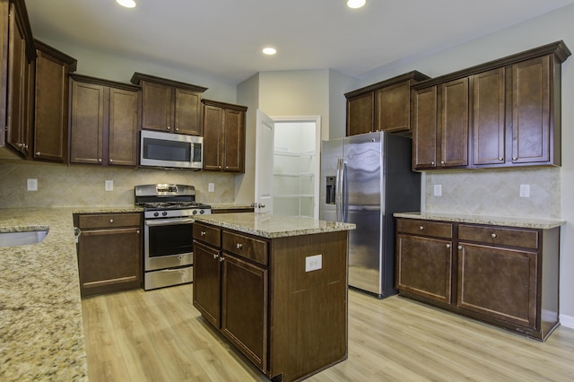 kitchen with appliances with stainless steel finishes, light hardwood / wood-style flooring, a center island, and light stone countertops