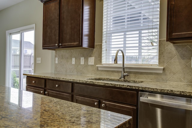 kitchen featuring light stone countertops, stainless steel dishwasher, backsplash, dark brown cabinets, and sink