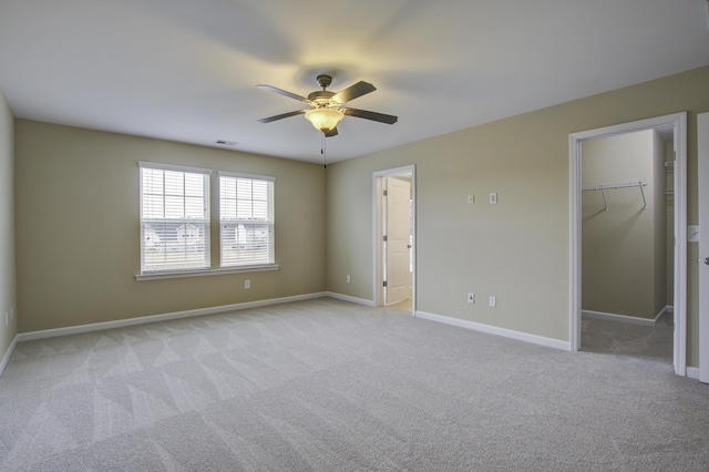 unfurnished bedroom featuring a walk in closet, light colored carpet, ceiling fan, and a closet