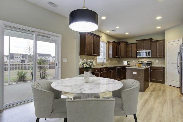 kitchen featuring stainless steel appliances, light stone counters, decorative backsplash, hanging light fixtures, and a kitchen island