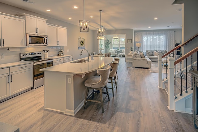 kitchen with a kitchen island with sink, light wood-style flooring, a sink, open floor plan, and appliances with stainless steel finishes